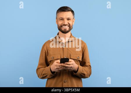 Smiling young man using smartphone and looking at camera Stock Photo