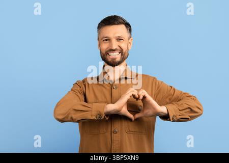 Smiling young man making heart shape with hands. Expressing love and kindness Stock Photo