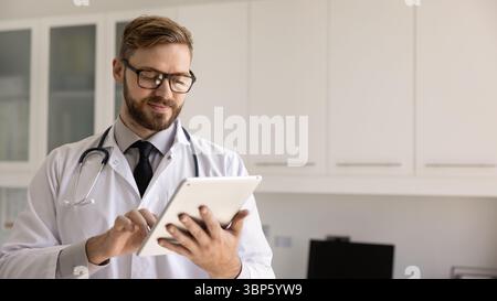 Focused positive young doctor man using digital tablet Stock Photo
