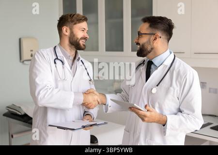 Two happy male doctors in lab coats shaking hands Stock Photo