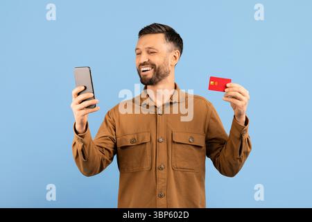 Online Shopping. Happy young man using phone and holding credit card Stock Photo