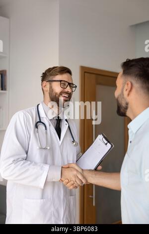 Positive young Caucasian doctor man shaking hands with patient, Stock Photo