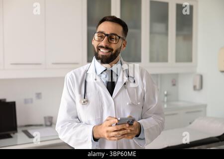Cheerful handsome Latin medical practitioner man holding mobile phone Stock Photo