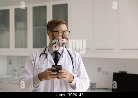 Happy cheerful young Caucasian medical expert using mobile phone Stock Photo