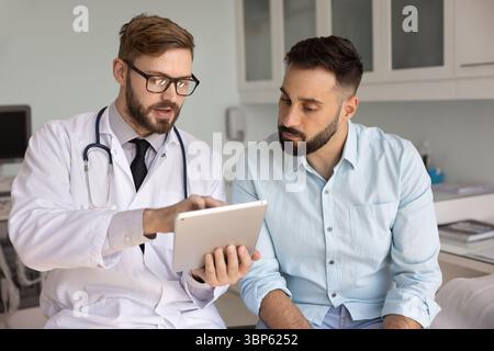 Serious doctor in glasses explaining electronic prescription to Latin man Stock Photo
