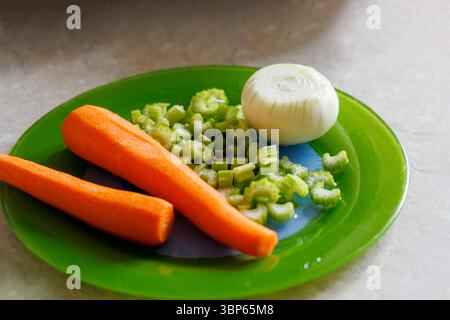 Fresh vegetables are displayed on a green plate, including two peeled carrots, chopped celery stalks, and half an onion. Stock Photo