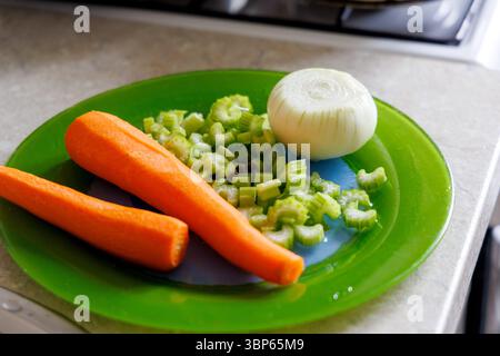 Fresh vegetables are displayed on a green plate, including two peeled carrots, chopped celery stalks, and half an onion. Stock Photo