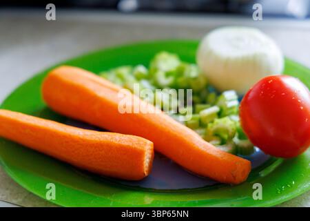 Fresh vegetables are displayed on a green plate, including two peeled carrots, chopped celery stalks, half an onion, and one tomato. Stock Photo