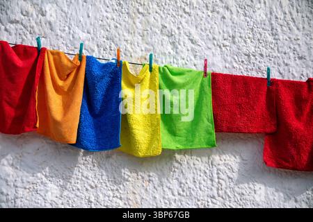 Cleaning cloths of various saturated colors hanging on a rope with clothespins on a white wall Stock Photo