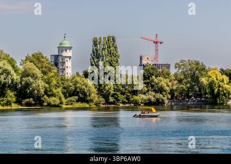 The water tower of the former Stromeyer tent factory in Stromeyersdorf, a district of Constance, Baden-Württemberg, Germany, rises above the trees. A modern building under construction with a crane stands to the right. Photographed from the Seerhein shore near Tägerwilen in the canton of Thurgau, Switzerland. Stock Photo