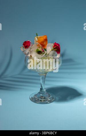 Colorful flowers in ice cubes in the glass on pastel blue background. Sunny day concept. Stock Photo