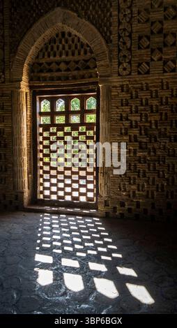 A beautifully designed wooden door with intricate patterns, casting geometric shadows on the stone floor. The sunlight filters through the door, illum Stock Photo