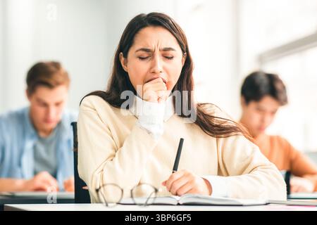 Female student yawning sitting at desk in class Stock Photo