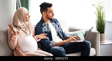 Annoyed pregnant muslim woman looking at husband that spending time with laptop Stock Photo