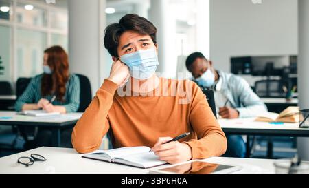 Asian male student in mask sitting at desk in class Stock Photo