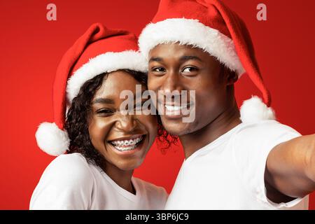 Beautiful black man and woman in Santa hats taking selfie Stock Photo