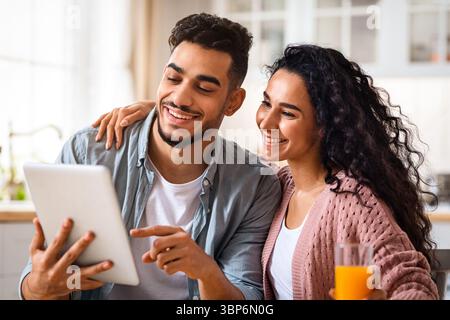 Loving Arab Couple Eating Breakfast Together And Using Digital Tablet In Kitchen Stock Photo