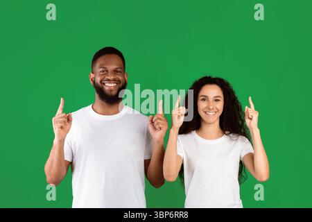 Diverse Couple Pointing Fingers Up Standing Over Green Background Stock Photo