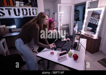 Two creative women collaborating in a studio, engaged in digital projects on a computer. The ambiance reflects a professional workspace with modern eq Stock Photo