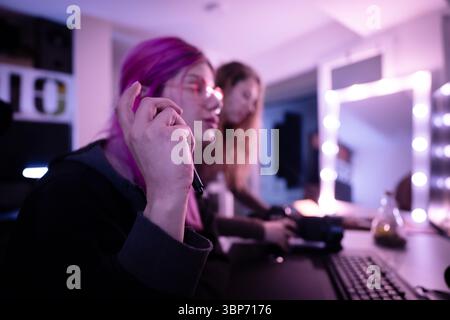 Creative workspace scene featuring two women focusing on a project, enhanced by pink and violet lighting, a desktop setup, and a stylish illuminated m Stock Photo