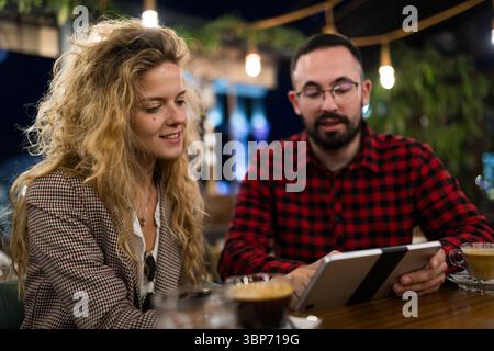 Two young professionals engage in a casual meeting with coffee in a cozy café, using a tablet for collaborative brainstorming and idea sharing. Stock Photo