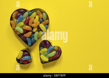 Multi-colored glazed jelly beans sweets in heart cookies molds on yellow backgrouns with copy space Stock Photo