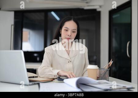 Businesswoman or female office worker is reading documents while sitting at working table in the office. Secretary or Clerk, Modern company. Stock Photo