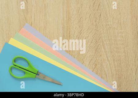 Top view of multicolored paper and scisors on wooden table. Top view. Arrangement for creative work or craft Stock Photo