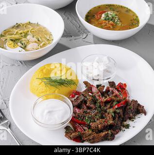 Food, Variety of delicious soups and a grilled meat dish, beautifully served on a textured white table, ready for dining Stock Photo