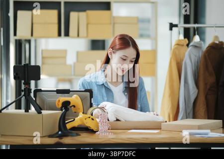 Smiling female entrepreneur packing clothing items for shipping in her startup workshop Stock Photo