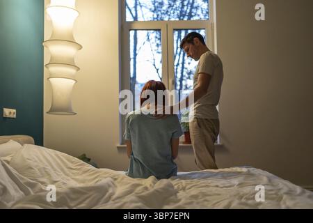 Sad woman sitting on bed near standing caring loving man husband touching wife shoulder. Comforting, apologising, thinking about relationship problems Stock Photo