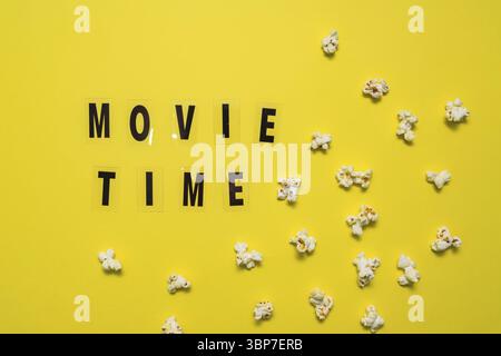 Movie Time text lettering with scattered salty popcorn on yellow background Stock Photo