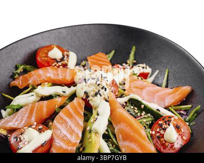 Food, Salmon salad with avocado, cherry tomatoes and arugula seasoned with sesame seeds and dressing on black plate Stock Photo