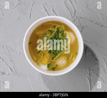 Food, Top view of a comforting bowl of chicken noodle soup garnished with parsley on a textured surface Stock Photo