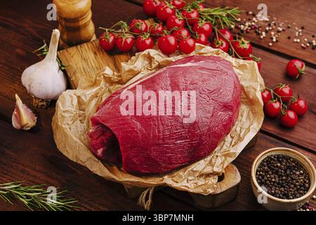 Food, A beautifully arranged display features a raw beef tenderloin wrapped in parchment on a wooden surface surrounded by cherry tomatoes, garlic, an Stock Photo