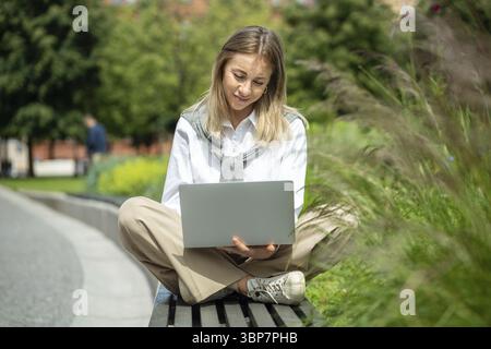 Contented girl using portable computer for communication, chat, job, professional activities, study. Glad girl resting relaxing in nature outside outd Stock Photo