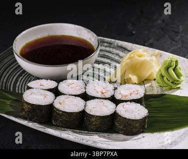 Food, Elegant presentation of sushi rolls with wasabi, ginger, and dipping sauce on a bamboo leaf and textured black background Stock Photo