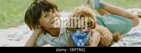 Biracial Child Boy Smiling While Lying on Blanket Outdoors with Dog Stock Photo
