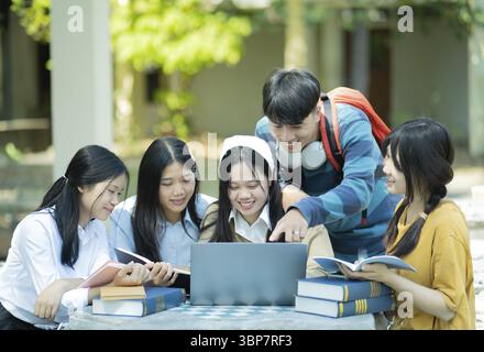 A group of college students studying together outdoors on campus, using a laptop and books in a collaborative setting Stock Photo