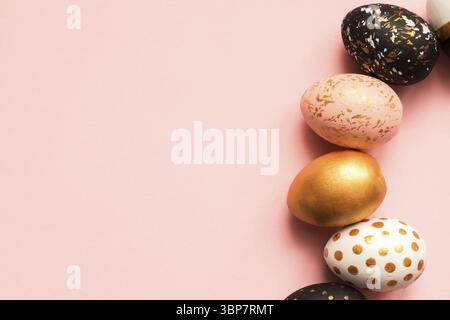 Frame made of wooden painted eggs in gold, black and rose colors on pink background. Happy easter background with copy space Stock Photo