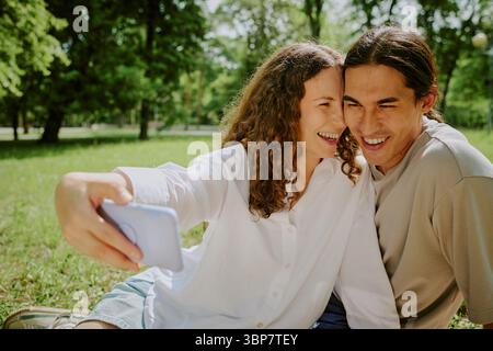 Young Caucasian Woman and Man Smiling While Taking Selfie in Park Outdoors Stock Photo