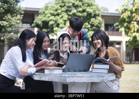 A group of college students studying together outdoors on campus, using a laptop and books in a collaborative setting Stock Photo