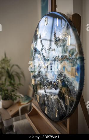 Majestic epoxy resin clock on easel. Huge round finished artwork masterpiece made in technique of fluid liquid art in marine sea ocean style. Gold wat Stock Photo