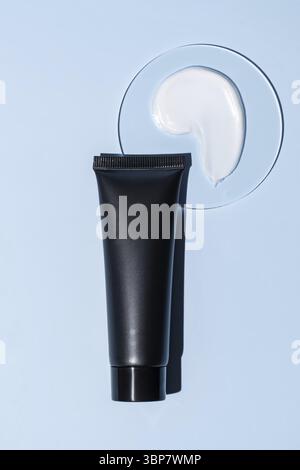 Black plastic squeeze tube of face or hand cream and sample texture in petri dish on blue background. Cosmetic laboratory research Stock Photo