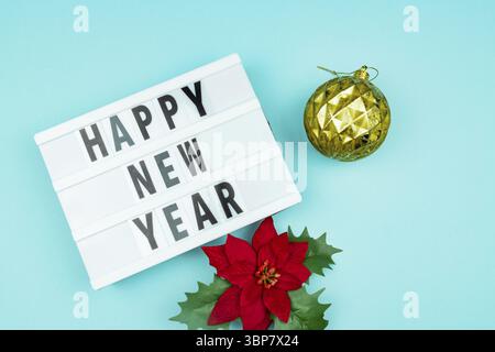 Happy new year light box with golden bauble and poinsettia on blue background Stock Photo