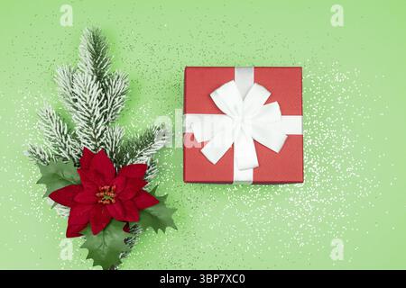 Top view of red gift box and fur tree branch with poinsettia on green background with confetti. Festive Christmas greeting card Stock Photo
