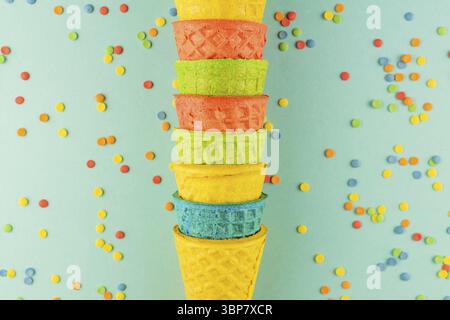 Bright multicolored ice-cream waffle cones on blue background with scattered confetti sugar sprinkles Stock Photo