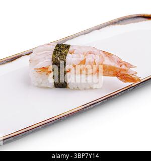 Food, A piece of sushi featuring a shrimp topping placed over a mound of rice, secured with a strip of seaweed, elegantly arranged on a white rectangu Stock Photo