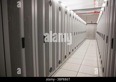 Server cabinets are receding into server room hallway in 3D render with raised floor tiles Stock Photo