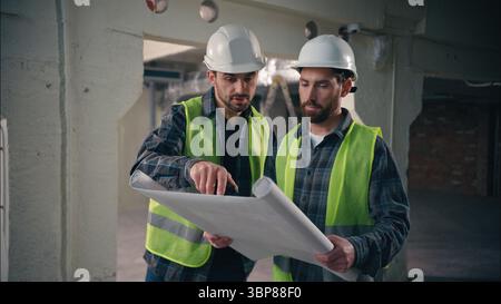 Professional Caucasian builders men holding blueprint building negotiation teamwork in construction architect control draft technicians discuss Stock Photo